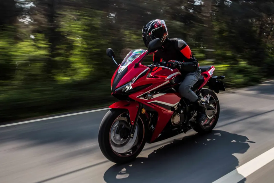 Motard sur une moto rouge en virage sur une route de campagne